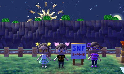 Beth, Jeff, and Squishy stand by the SNF sign as fireworks go off in the sky.
